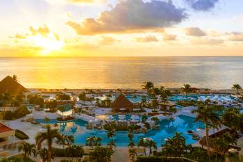 Sunset aerial view of Moon Palace Cancun pools and beachfront with palm trees and ocean horizon