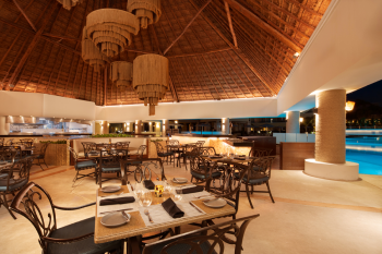 Open-air dining area at Palapa Asadero restaurant at Moon Palace Cancun with thatched roof and poolside seating