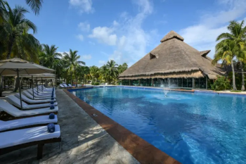 Main pool at El Dorado Royale Riviera Maya
surrounded by tropical landscaping, lounge chairs, and a thatched-roof building
in Riviera Maya, Mexico.